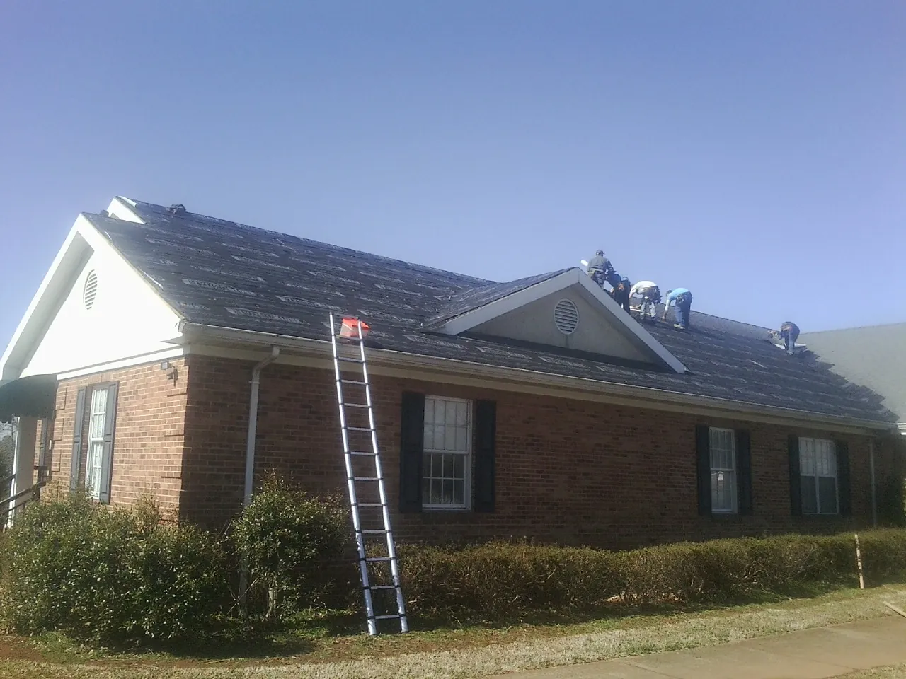Crew tearing shingles off a brick ranch roof with a ladder set — Emergency Roof Repair work by our crew in Norco