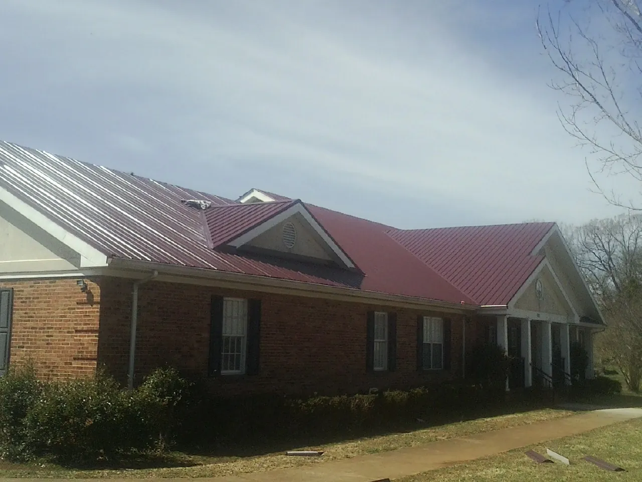 Red metal roof with gabled entries on a long brick building, from a Hail Damage Roof Repair job in Norco
