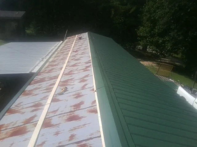 Old rusted panels beside newly installed green metal roofing — Wind Damage Roof Repair by Roofing Brothers in Norco
