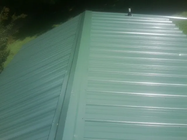 New green metal panels meeting at the ridge of a roof — Flat Roof Repair work by our crew in Norco