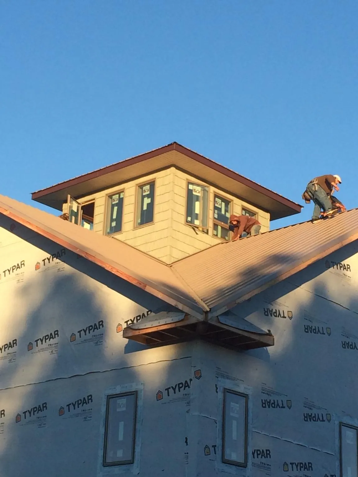 Roofers working around a rooftop cupola on a new metal roof at sunset — Roof Waterproofing in Norco by Roofing Brothers